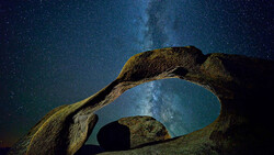 Milky Way galaxy framed through a natural stone arch formation against a starry night sky.