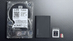 WD Black 4TB hard drive with external SSD, memory card, and microSD card on carbon fiber surface.