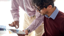 Two people examining a tablet together in an office setting with natural lighting.