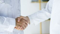 Two healthcare professionals in white coats shaking hands.