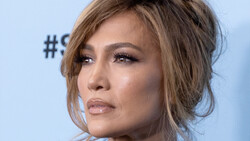 Woman's face in profile against a light blue background, showcasing soft portrait lighting and makeup.