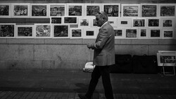 Man in suit walking past wall of black and white photographs in gallery setting.