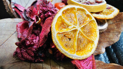 Dried citrus slices and dried flower petals arranged on a wooden surface.