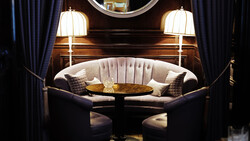 Symmetrical luxury lounge seating with curved cream-colored banquette, round table, pendant lamps, and dark curtains.