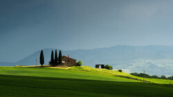 Tuscan villa with cypress trees on rolling green hillside under hazy sky.