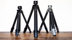 Three carbon fiber camera tripods of varying heights arranged in a row on a wooden surface.