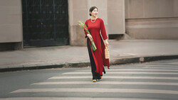 Woman in red áo dài walking across a crosswalk while carrying palm leaves and a woven basket.