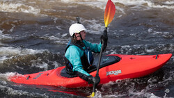 Whitewater kayaker in bright red kayak navigating turbulent rapids while holding yellow and red paddle.