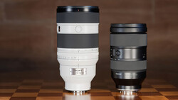 Two telephoto camera lenses side by side on a wooden surface against a brown backdrop.