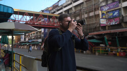 Photographer holding camera to face while standing in urban amusement park setting.