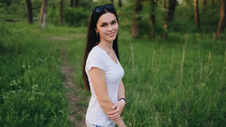 Woman in white t-shirt standing on a forest path with sunglasses on her head.