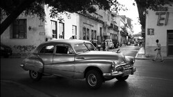 1950s sedan parked on a street lined with colonial-era buildings in a tropical location.