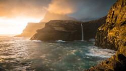Waterfall cascading down golden cliffs into turquoise ocean waters during golden hour sunset.