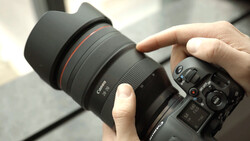 Photographer's hands holding a Canon RF-mount telephoto lens attached to a mirrorless camera body.