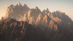 Dramatic jagged mountain peaks bathed in golden sunrise light with deep shadows in the valleys.
