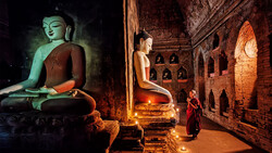 Buddhist statue illuminated in green light inside a candlelit temple chamber with brick walls.