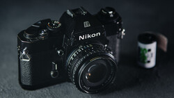 Black Nikon DSLR camera with attached lens on dark textured surface.