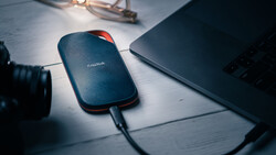 SanDisk portable external hard drive connected to laptop on white desk workspace.