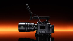 Professional cinema camera with attached lens and microphone against warm orange gradient backdrop.