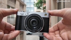 Hands holding a silver and black rangefinder camera with fixed lens against urban background.