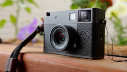 Vintage rangefinder film camera with gray and black body sitting on wooden surface with plants in background.