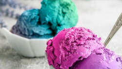 Scoops of vibrant magenta and turquoise ice cream in white bowls with a metal spoon.