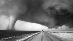 Tornado touching down across flat plains with a straight road leading toward the storm under dark clouds.
