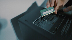 Hands installing a RAM module into a laptop's memory slot.