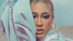 Woman with shaved head wearing purple eyeshadow and draped mint green fabric with magenta stripes.
