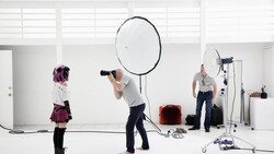 Photography studio setup with large reflector, model, and lighting equipment on white cyclorama.