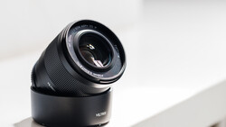 Black telephoto lens with hood mounted on white surface in bright daylight.