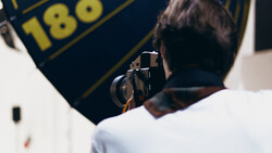 Photographer holding a camera while framing a shot of a navy banner with gold text and numbers.