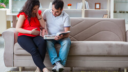 Couple sitting on a gray sofa reviewing documents together in a bright living room.