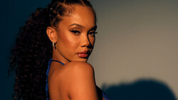Woman with long curly hair looking over shoulder against blue and warm lighting backdrop.