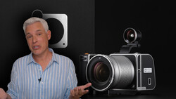 Man in striped shirt discussing camera equipment displayed against black background.