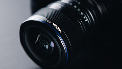 Wide-angle camera lens with blue accent ring mounted at an angle against a neutral gray background.