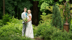 Bride and groom posing together in a lush garden setting with greenery and trees in the background.