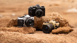 Three mirrorless cameras in different colors arranged on sandy rocks in desert terrain.