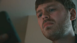 Man with stubble looking downward with concerned expression against neutral background.
