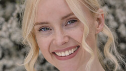 Blonde woman with wavy hair smiling at camera against textured gray background.