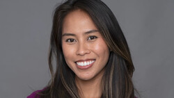 Woman with long dark hair smiling at camera against neutral gray background.