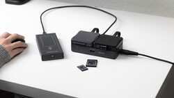Desktop setup showing a contactless card reader, dual battery chargers, and memory cards on a white desk.