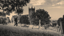 Sepia-toned cemetery scene with stone church and gravestones framed by overhanging trees.