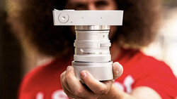 Hands holding a vintage rangefinder camera lens assembly with chrome barrel and focusing mechanism.