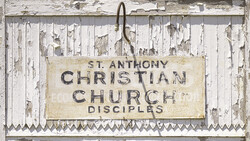Weathered wooden sign for St. Anthony Christian Church Disciples with peeling white paint and metal frame.