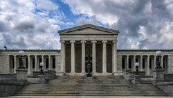 Neoclassical museum building with columned portico and symmetrical wings under partly cloudy sky.