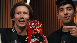 Two men in black clothing holding a red box product, smiling at camera in studio setting.