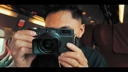 Photographer holding a teal rangefinder camera up to eye level, shot from inside a vehicle with warm interior lighting.