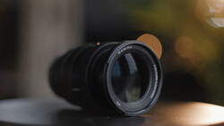 Prime lens with dark glass elements and manual focus ring, photographed on a neutral surface with soft bokeh background.