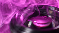 Macro shot of camera lens elements with magenta and purple lighting and motion blur effects.